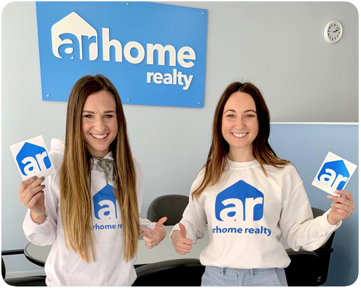 two people standing in ar logo sweaters holding ar logo stickers; linking to why arhome