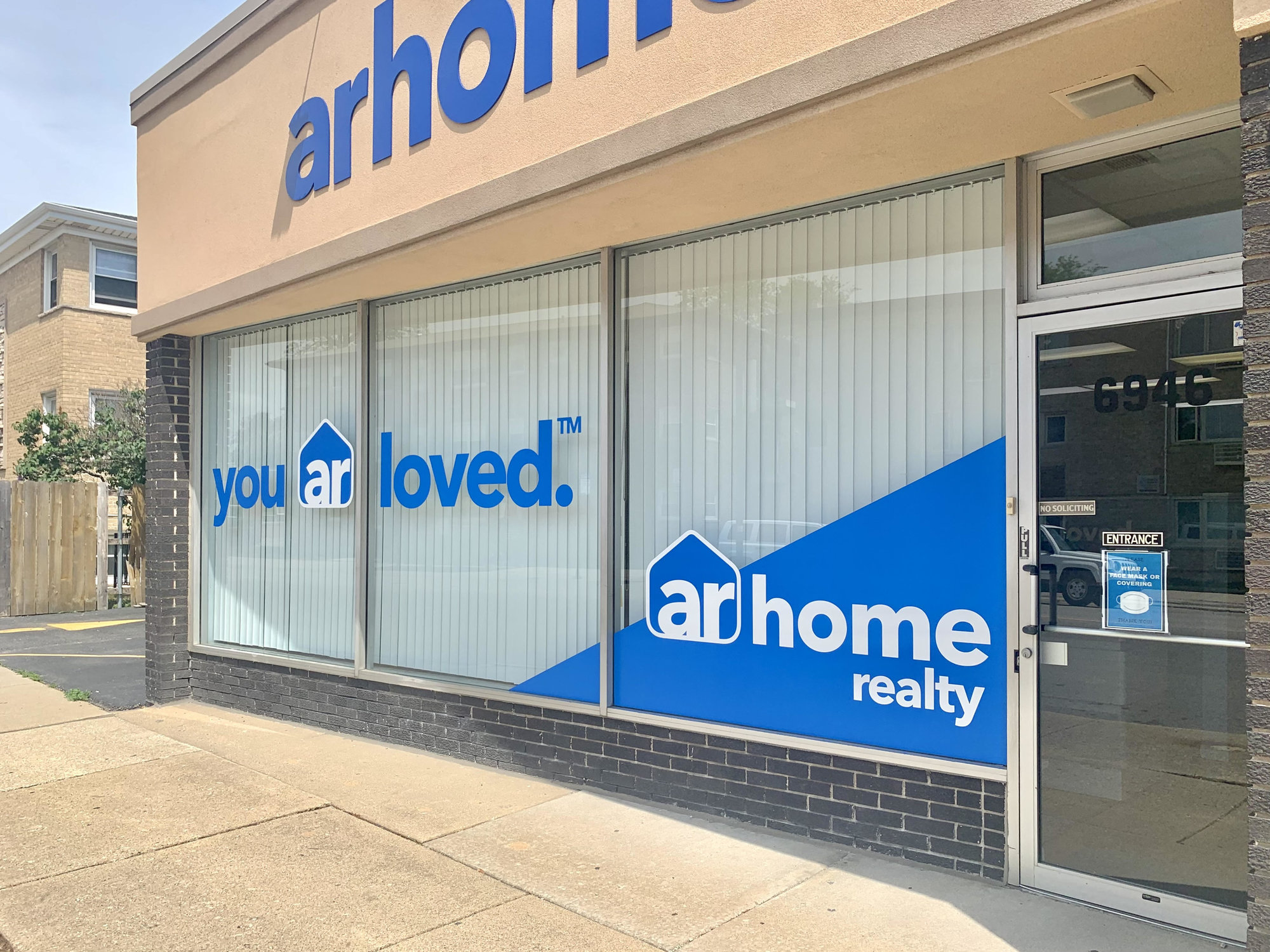 photo of the front of the office of arhome realty with decal on the windows saying 'you ar loved' and part of the top of the arhome realty sign showing higher on the building